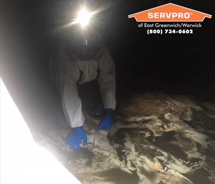 A person in PPE in a crawl space. 